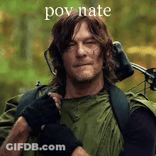 A Man In A Green Jacket Is Holding A Bow And Arrow And Wearing Headphones . GIF