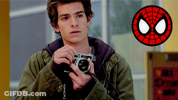 A Man In A Green Jacket Is Holding A Camera In Front Of A Spider Man Logo GIF