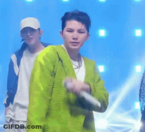 A Man In A Green Jacket Is Holding A Microphone While Standing On A Stage . GIF
