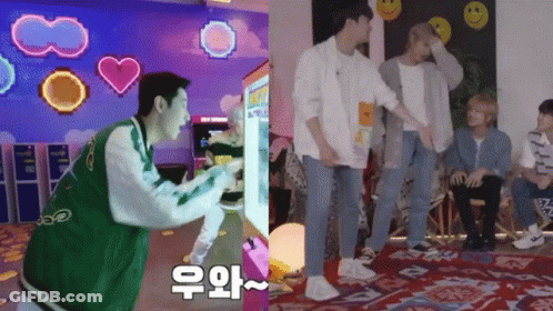 A Man In A Green Jacket Is Playing A Video Game Next To A Group Of Young Men GIF