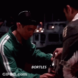 A Man In A Green Jacket Is Sitting At A Table Talking To Another Man With The Word Bortles Above Him . GIF