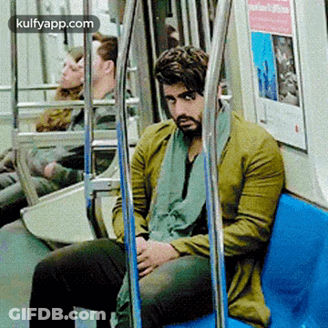 A Man In A Green Jacket Is Sitting On A Blue Bench On A Subway Train . GIF