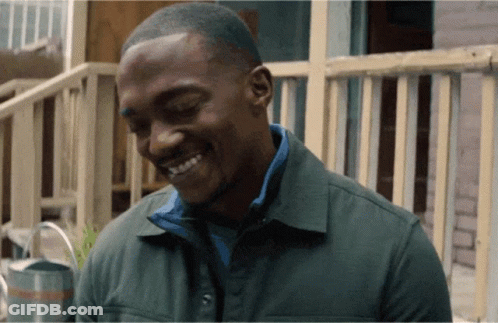 A Man In A Green Jacket Is Smiling In Front Of A Railing GIF