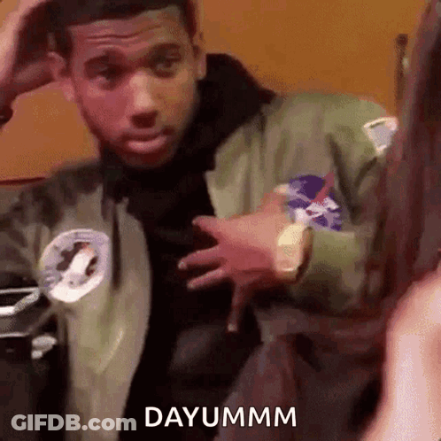 A Man In A Green Jacket Is Standing In Front Of A Woman And Holding His Hand To His Head . GIF