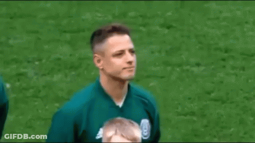 A Man In A Green Jacket Is Standing On A Soccer Field And Smiling . GIF