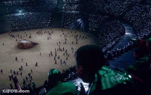 A Man In A Green Jacket Looks At A Crowd Of People GIF