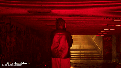 A Man In A Green Jacket Stands In A Dark Tunnel With The Words #Clayfacemovie Below Him GIF