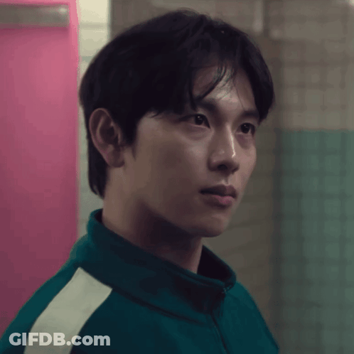 A Man In A Green Jacket Stands In Front Of A Pink Wall GIF