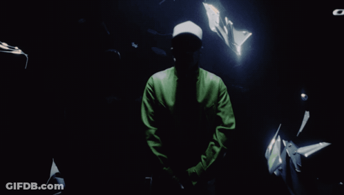 A Man In A Green Jacket Stands In The Dark GIF
