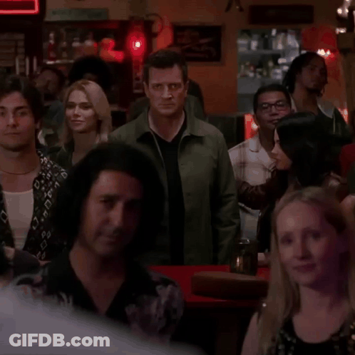 A Man In A Green Jacket Stands In The Middle Of A Crowd GIF