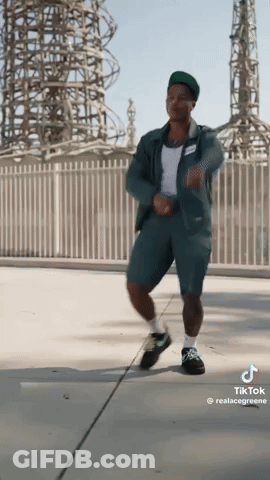 A Man In A Green Jumpsuit Is Dancing On A Sidewalk GIF