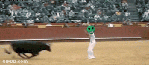 A Man In A Green Mask Stands In Front Of A Bull In A Bullring GIF