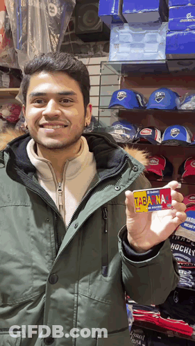 A Man In A Green Parka Holds Up A Card That Says Tabana GIF