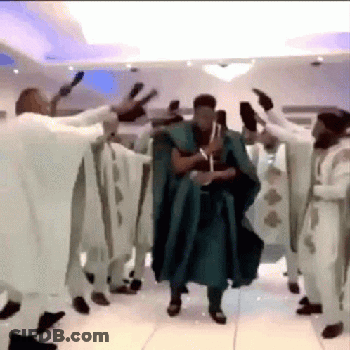 A Man In A Green Robe Is Dancing With A Group Of Men In White Robes . GIF