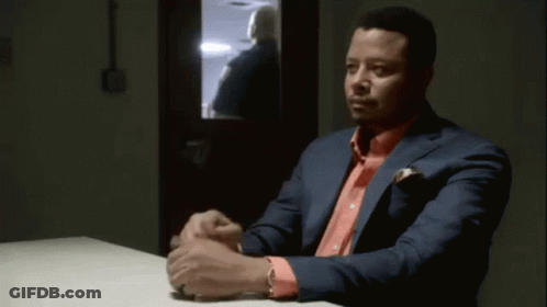 A Man In A Green Scrub Top Is Sitting At A Table With Another Man . GIF