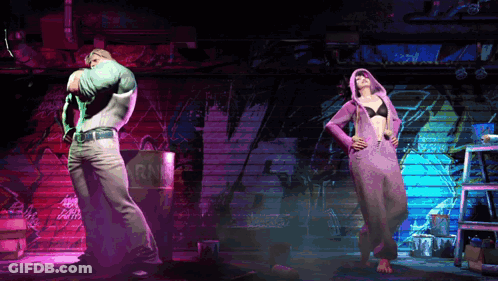 A Man In A Green Shirt And A Woman In A Purple Hoodie Are Dancing In A Dark Room GIF