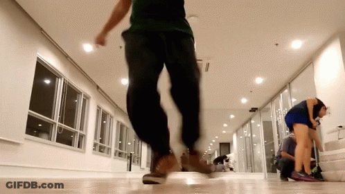 A Man In A Green Shirt And Black Pants Is Walking In A Hallway GIF