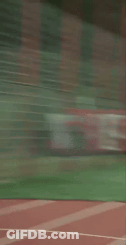 A Man In A Green Shirt And Black Shorts Is Standing On A Track GIF