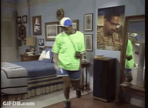 A Man In A Green Shirt And Blue Shorts Is Standing In A Bedroom . GIF