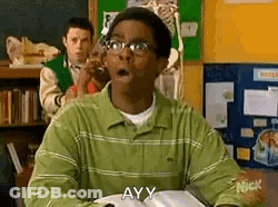 A Man In A Green Shirt And Glasses Is Sitting At A Desk In A Classroom With His Mouth Open . GIF
