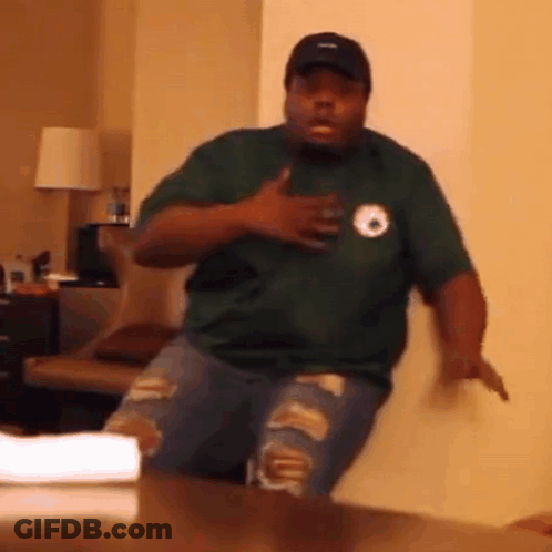 A Man In A Green Shirt And Ripped Jeans Is Standing In Front Of A Table . GIF