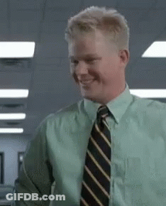 A Man In A Green Shirt And Tie Is Smiling And Looking At The Camera . GIF