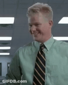 A Man In A Green Shirt And Tie Is Smiling And Looking At The Camera . GIF