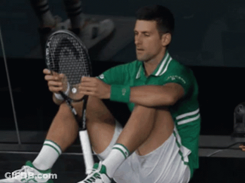 A Man In A Green Shirt And White Shorts Sits On The Floor Holding A Head Tennis Racquet GIF