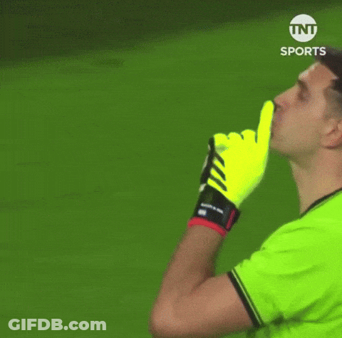 A Man In A Green Shirt And Yellow Gloves Is Making A Shhh Gesture . GIF