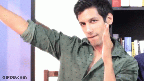 A Man In A Green Shirt Has His Arm Outstretched In Front Of A Bookshelf GIF