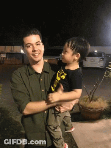 A Man In A Green Shirt Holds A Little Boy In A Black Shirt That Says ' A ' On It GIF