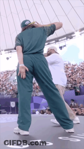 A Man In A Green Shirt Is Dancing In Front Of A Crowd With The Number 2 On The Floor GIF