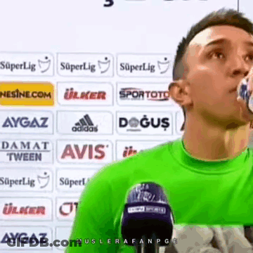 A Man In A Green Shirt Is Drinking Water From A Bottle . GIF