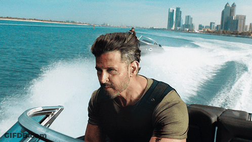 A Man In A Green Shirt Is Driving A Boat In The Ocean GIF