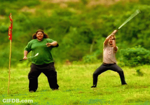 A Man In A Green Shirt Is Holding A Sword In A Field GIF