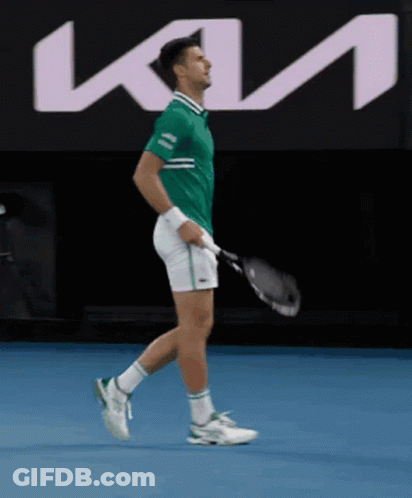 A Man In A Green Shirt Is Holding A Tennis Racquet In Front Of A Kia Sign GIF