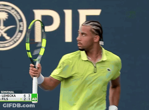 A Man In A Green Shirt Is Holding A Tennis Racquet In Front Of A Sign That Says " It " GIF