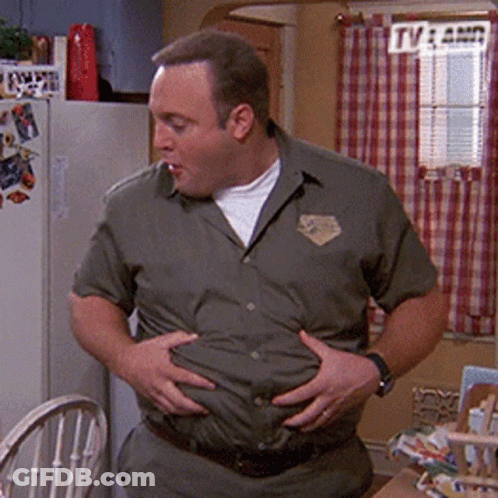 A Man In A Green Shirt Is Holding His Belly In A Kitchen . GIF