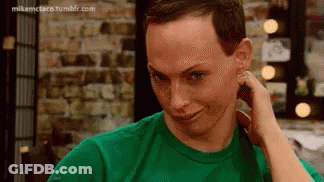 A Man In A Green Shirt Is Holding His Hand To His Ear And Making A Funny Face . GIF
