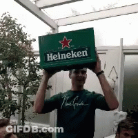 A Man In A Green Shirt Is Holding Up A Box Of Heineken GIF
