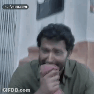 A Man In A Green Shirt Is Laughing While Holding A Pink Object In His Hand . GIF