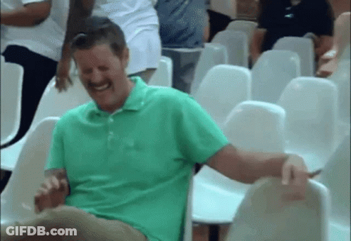 A Man In A Green Shirt Is Laughing While Sitting In A Row Of Chairs . GIF