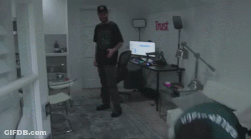 A Man In A Green Shirt Is Laying On The Floor Next To A Broken Monitor . GIF