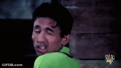 A Man In A Green Shirt Is Making A Funny Face In Front Of A Sign That Says ' Sword League ' GIF