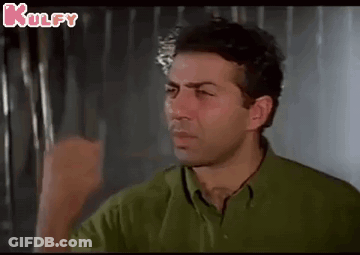 A Man In A Green Shirt Is Making A Funny Face While Holding His Fist Up . GIF