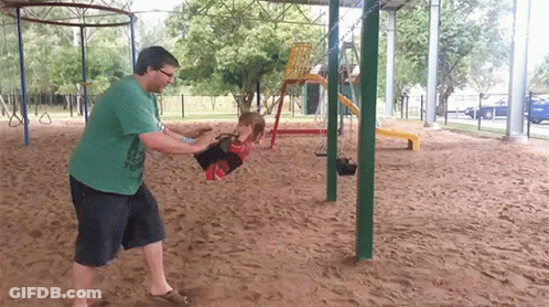 A Man In A Green Shirt Is Pushing A Little Girl On A Swing GIF