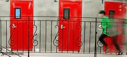 A Man In A Green Shirt Is Running Across A Balcony With Red Doors In The Background . GIF