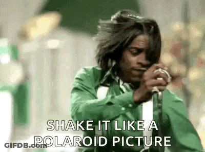 A Man In A Green Shirt Is Singing Into A Microphone And Saying Shake It Like A Polaroid Picture . GIF