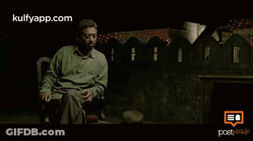 A Man In A Green Shirt Is Sitting In Front Of A Fence With The Website Kulfyapp.com On The Bottom Right GIF