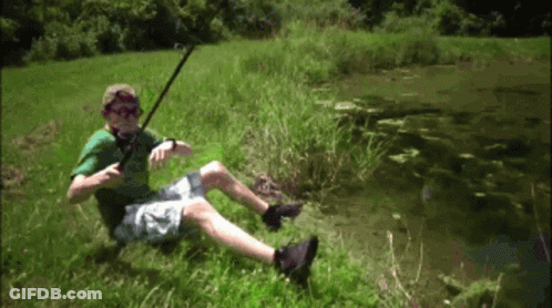 A Man In A Green Shirt Is Sitting In The Grass Holding A Fishing Rod GIF